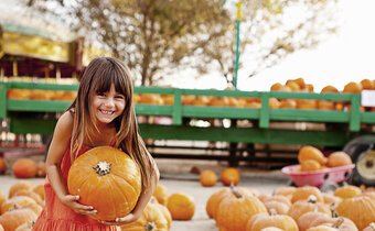 Little girl picking up pumpkin